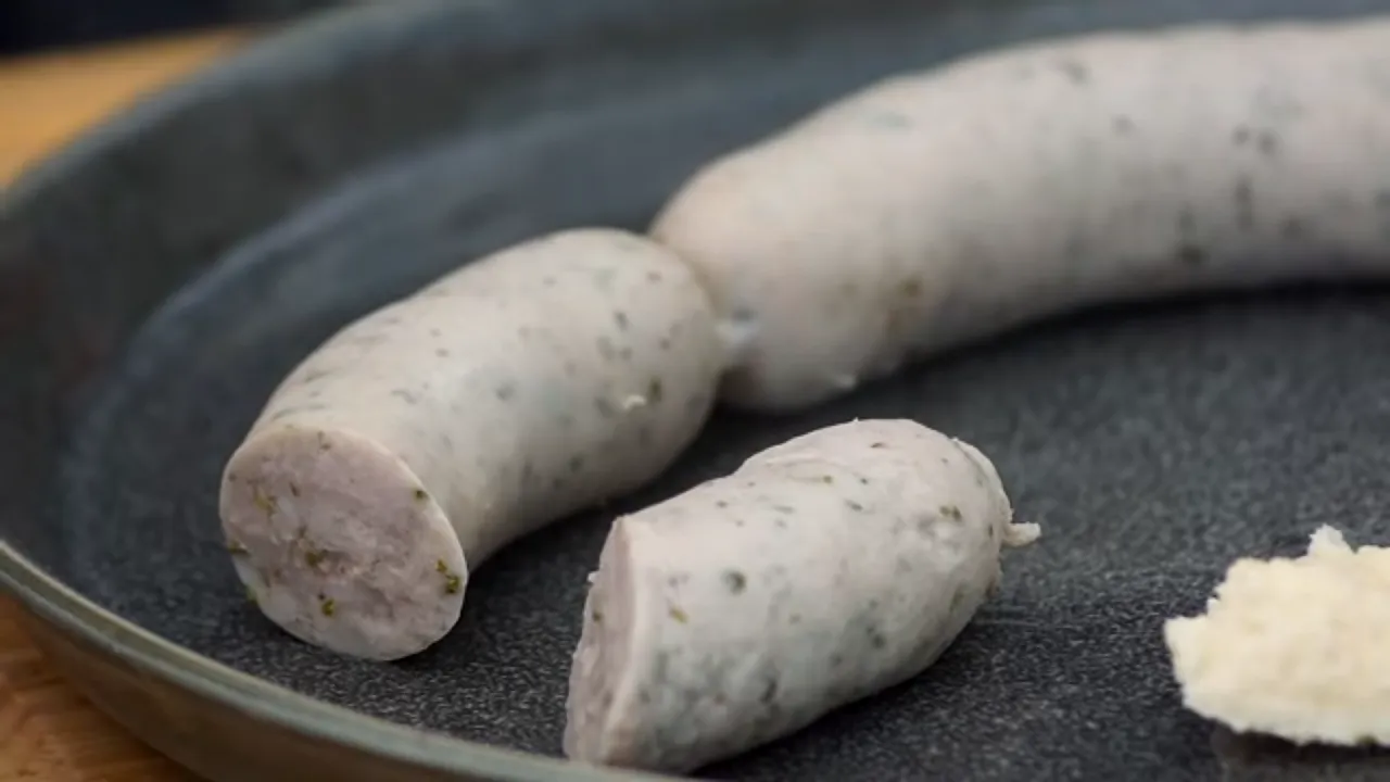 Biała kiełbasa w naczyniu, gotowa do parzenia. Pokrojony kawałek pokazuje jej delikatne wnętrze z ziołami.