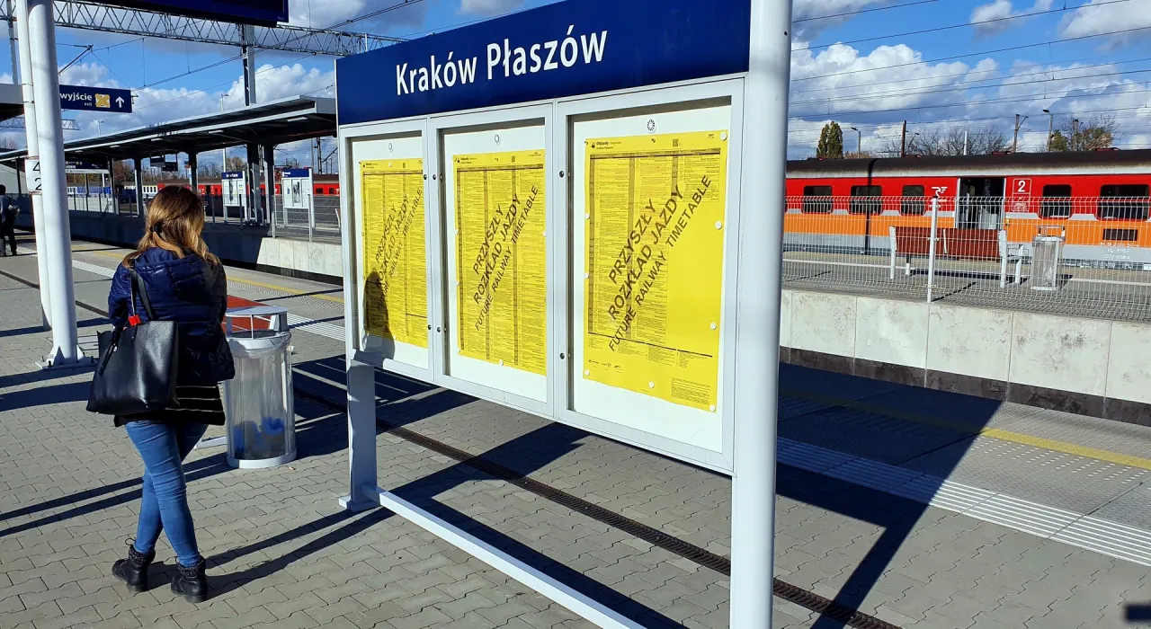 Kobieta czeka na pociąg na stacji Krak&oacute;w Płasz&oacute;w. Sprawdza rozkład jazdy, by dowiedzieć się, z jakiego peronu odjeżdża pociąg.