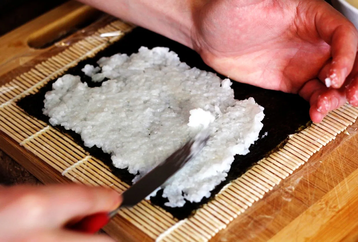 Ręce rozprowadzają ryż na nori, przygotowując się do nauki, jak zawijać sushi.