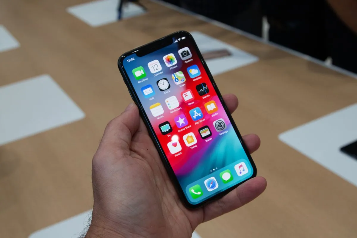 Dłoń trzyma smartfon z kolorowym ekranem, na kt&oacute;rym widać ikony aplikacji. Czy to iPhone X czy XS?