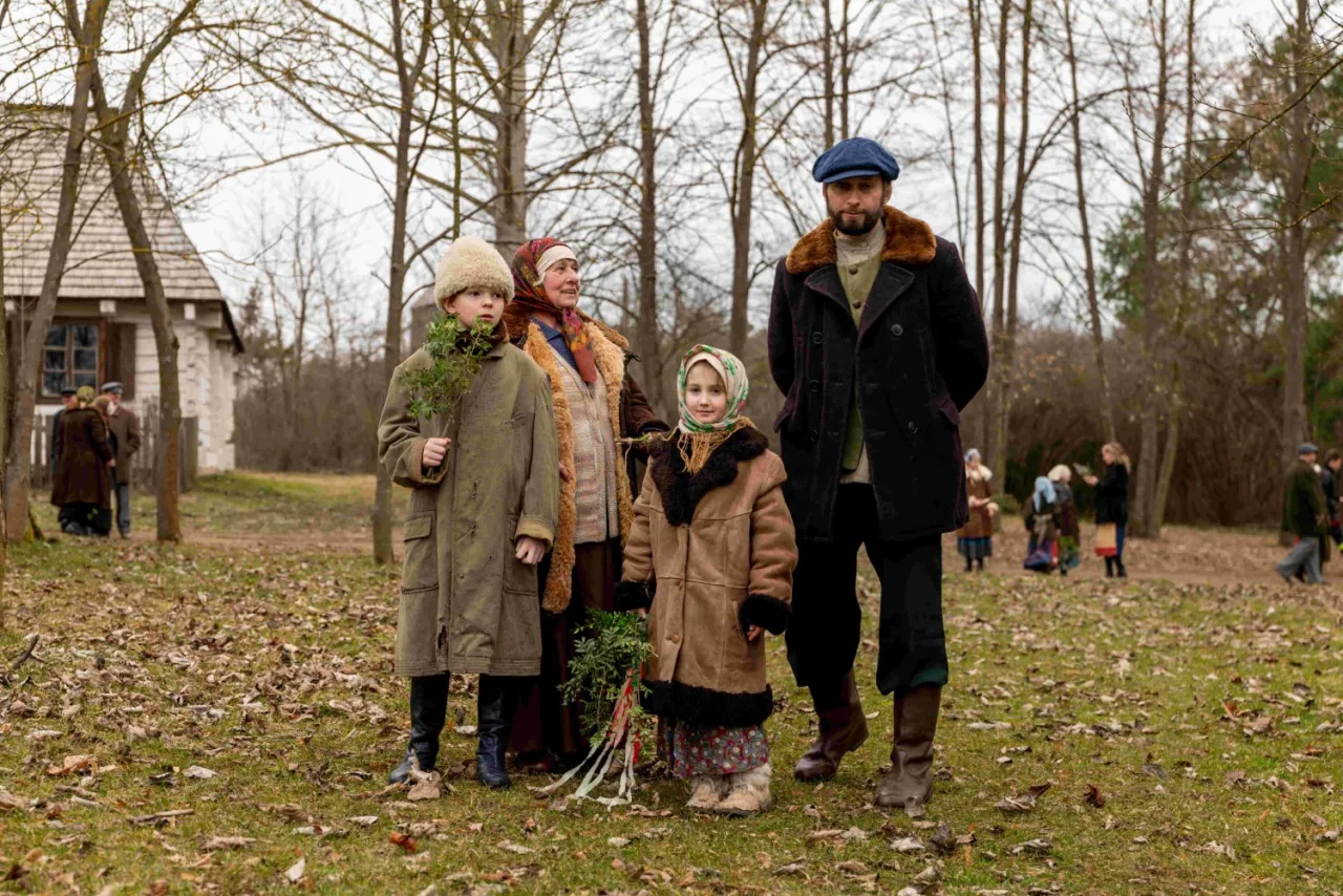 Rodzina Pawlaków: ojciec, matka, babcia i dwoje dzieci, pozują do zdjęcia na tle wiejskiego krajobrazu.