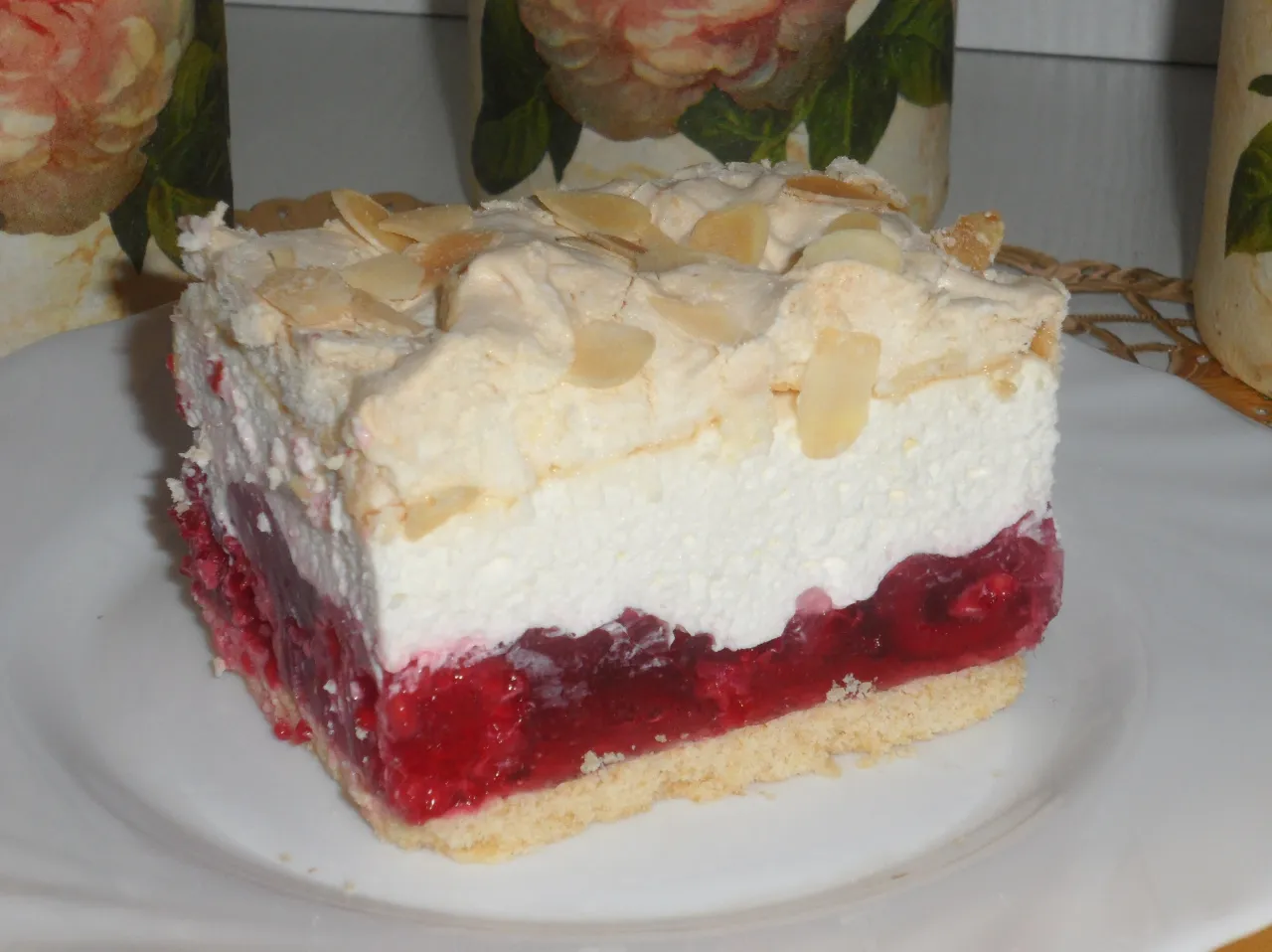 Pyszny kawałek ciasta malinowa chmurka z chrupiącą bezą i migdałami. Idealny deser, gdy zastanawiasz się, jak zrobić bezę na ciasto malinowa chmurka.