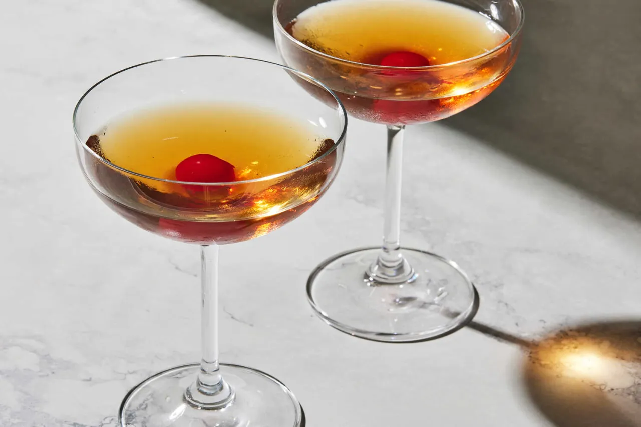Dwa kieliszki z bursztynowym drinkiem i wiśnią. Klasyczny Manhattan na słodkim czy na wytrawnym wermucie?