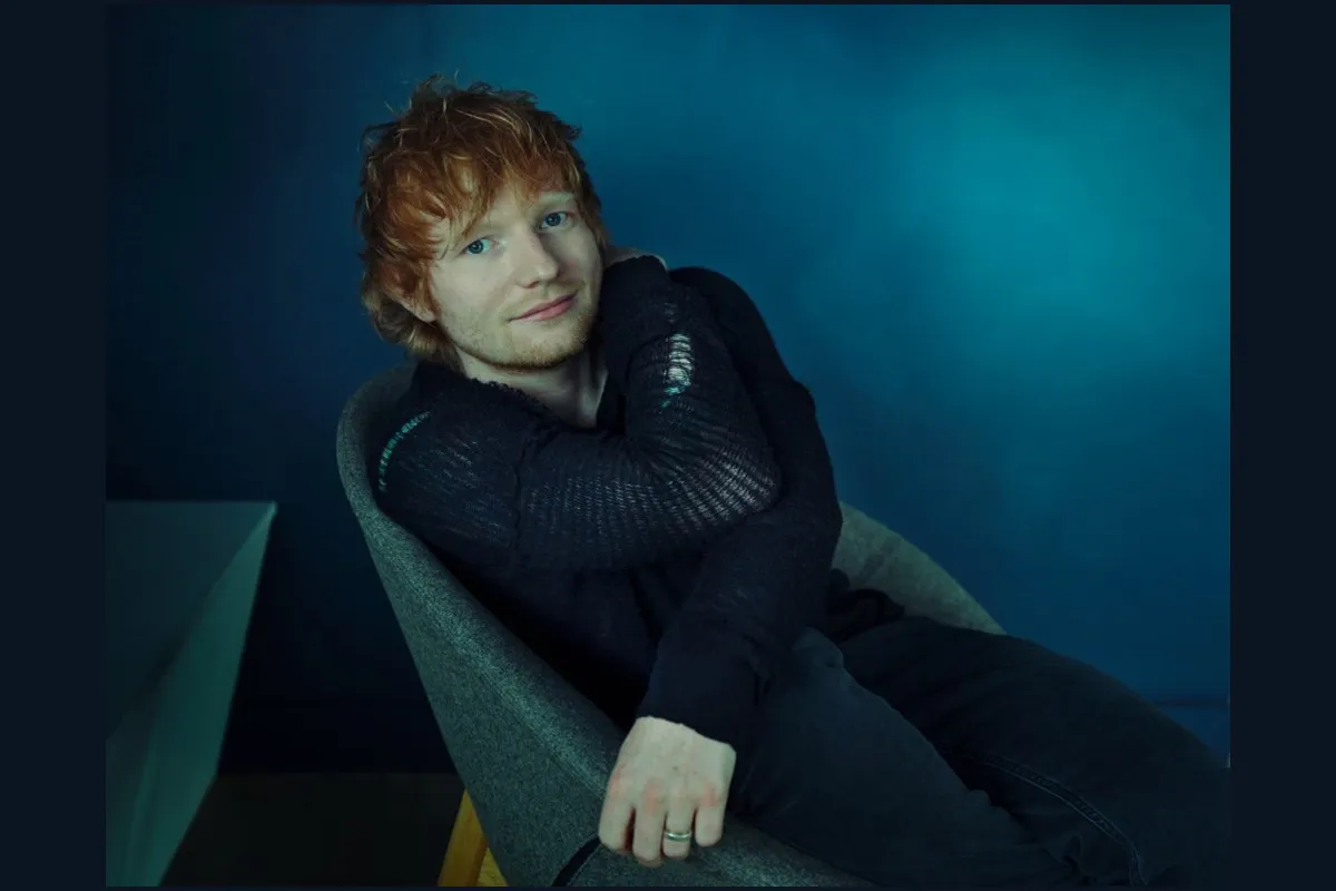 Ed Sheeran, z rudymi włosami i niebieskimi oczami, siedzi w fotelu. Czy Ed Sheeran grał w Harrym Potterze? Nie, ale jego uśmiech mógłby rozjaśnić Hogwart.