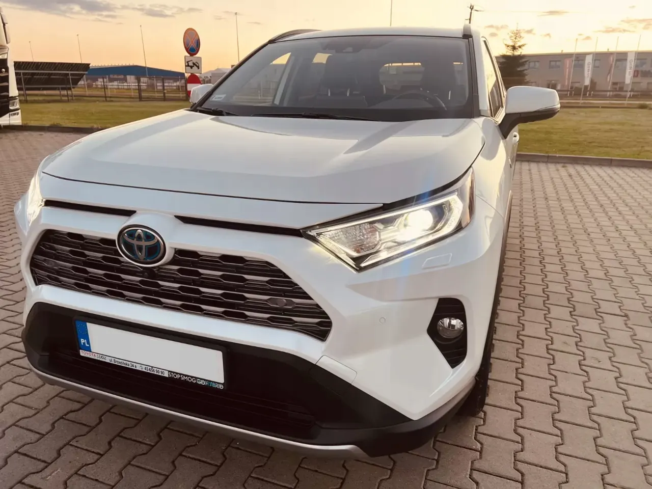 Biała Toyota RAV4 hybrydowa zaparkowana na kostce brukowej. Zastanawiasz się, ile kosztuje Toyota? Ten model to świetny wyb&oacute;r.