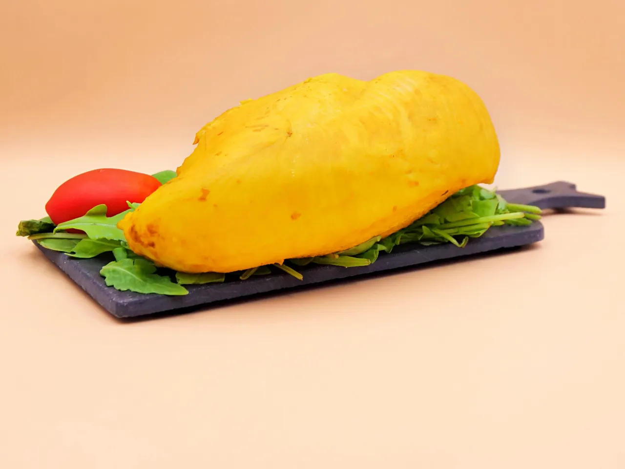 Gotowa do podania, żółta pierś z kurczaka na ciemnej desce z rukolą i pomidorkiem. Idealna do szybkiego obiadu, zastanawiasz się, ile czasu gotować pierś z kurczaka?