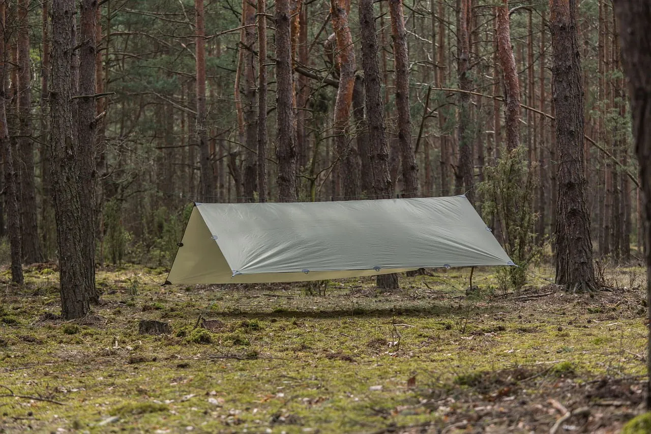 Jak rozłożyć namiot typu tarp w lesie? Lekki, zielony tarp rozwieszony między drzewami, tworząc schronienie.