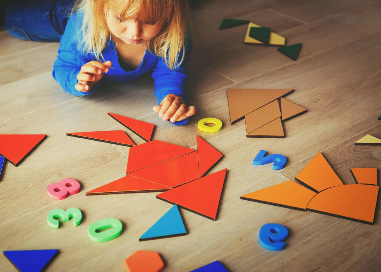 Mała dziewczynka układa kolorowe kształty i cyfry. To świetna zagadka dla dziecka, rozwijająca kreatywność i logiczne myślenie.