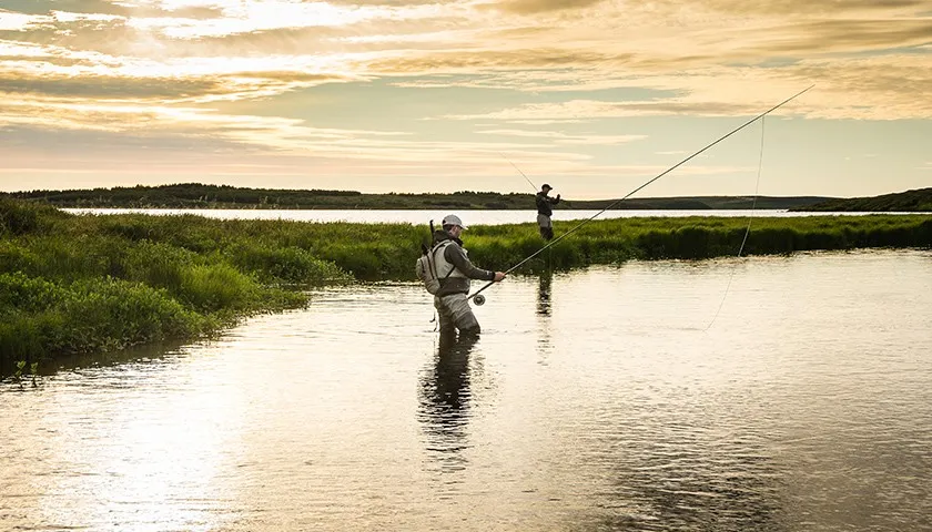 Wędkarz łowiący spinningiem z brzegu i wędkarz łowiący z łodzi, pokazujące r&oacute;żnice w długości wędki