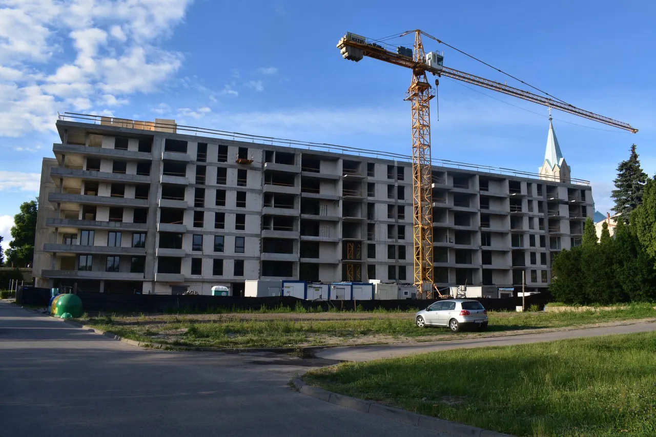 Budowa bloku mieszkalnego, gdzie można dowiedzieć się, jak dostać mieszkanie od spółdzielni. Dźwig budowlany i kościół w tle.