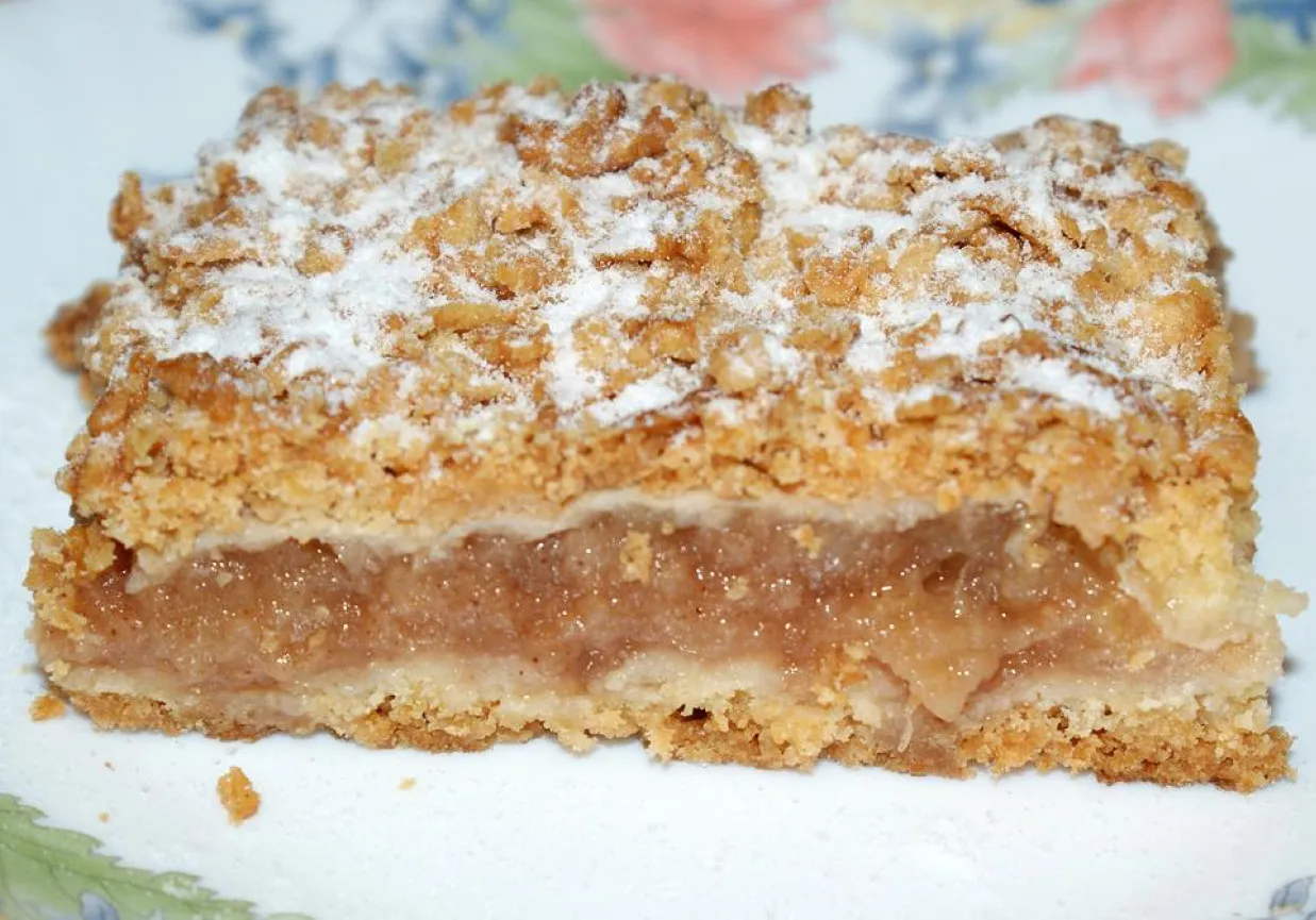 Kawałek szarlotki z kruszonką, posypany cukrem pudrem. Idealna na deser, a jak przechowywać szarlotkę? Najlepiej w szczelnym pojemniku.