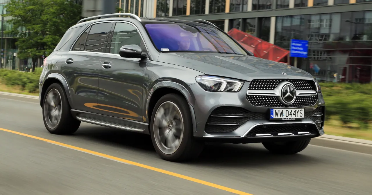 Szary Mercedes GLE 300 d w ruchu miejskim, z widocznym kierowcą za kierownicą.