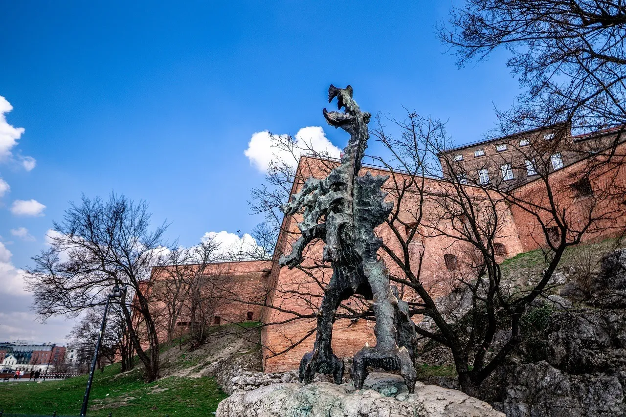 Pomnik Smoka Wawelskiego, bohatera słynnej baśni, stoi dumnie na tle ceglanych murów zamku.