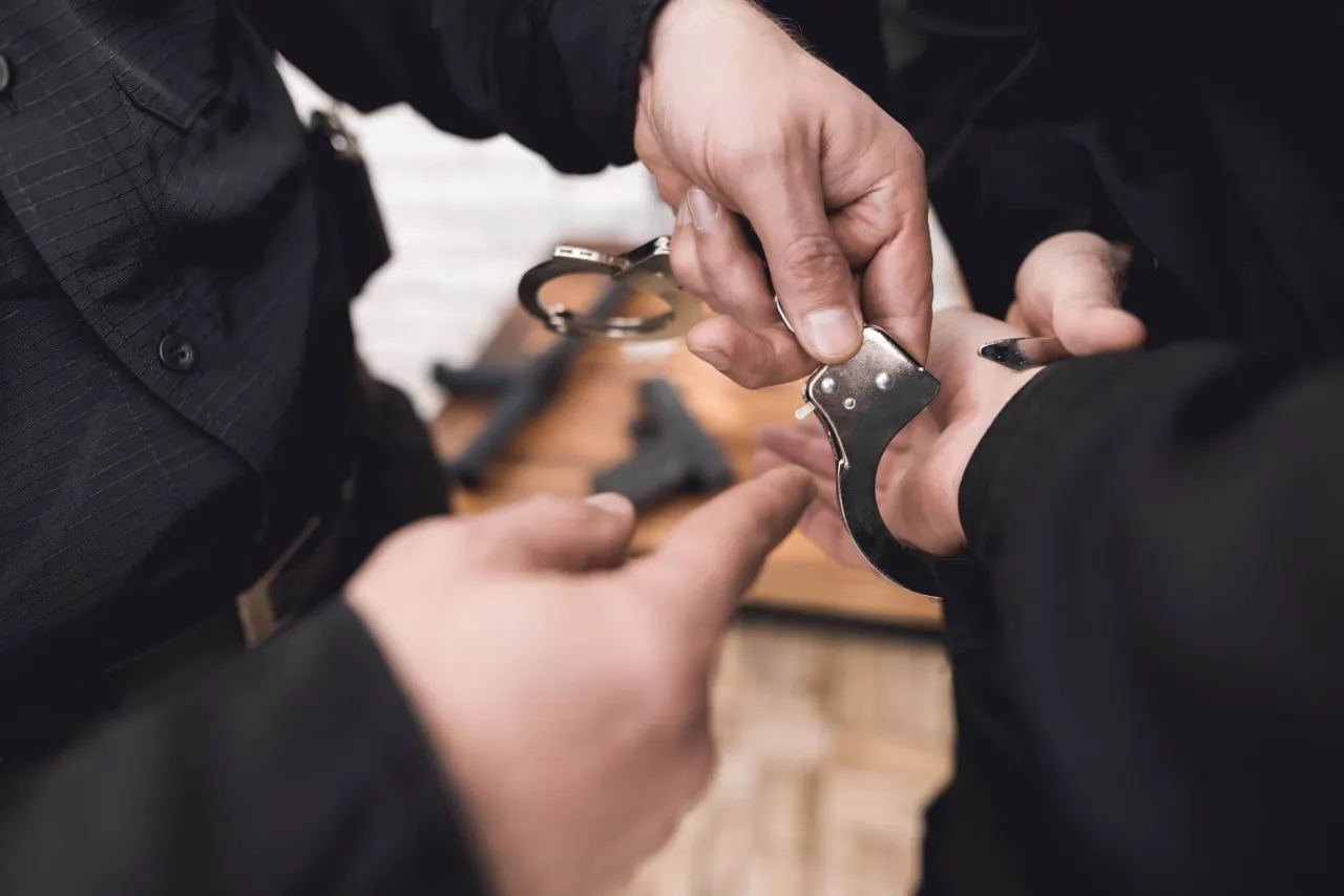 Dłoń policjanta zakłada kajdanki. Czy policjant po służbie może wystawić mandat? Pytanie pozostaje otwarte.