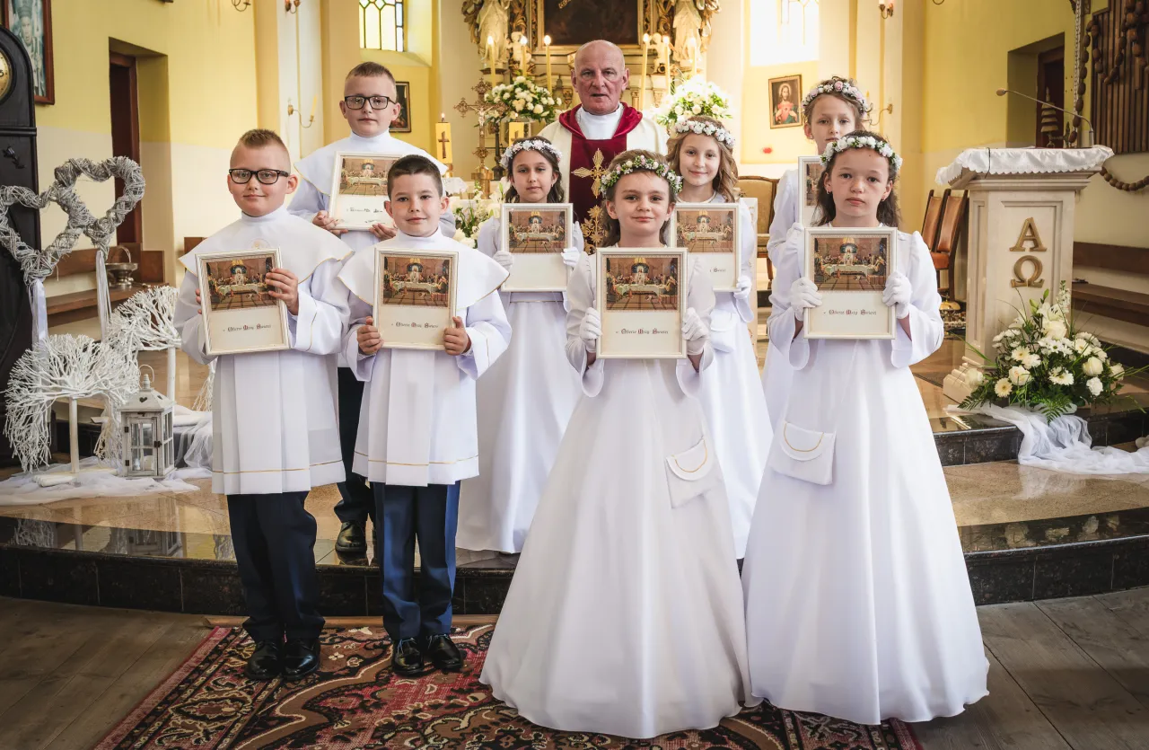 Dzieci w bieli po Komunii Świętej, z księdzem. Zastanawiasz się, ile kosztuje fotograf na komunie?