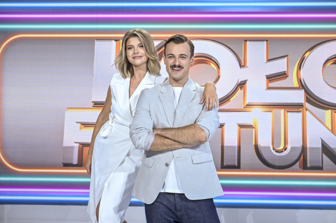 Poznaj nową prowadzącą Koło Fortuny! Uśmiechnięta para na tle neonowego logo programu.