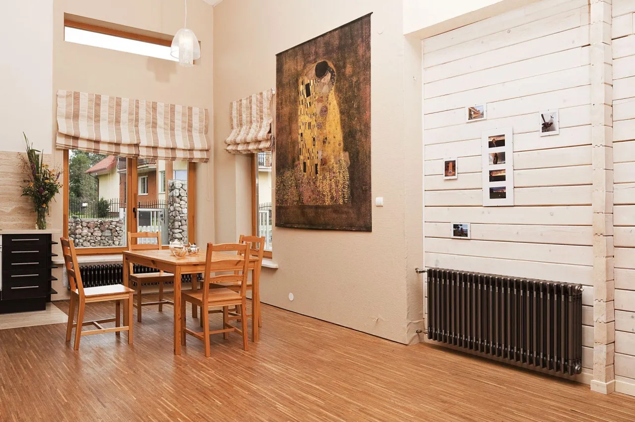 Duży, czarny grzejnik żeliwny przy drewnianej ścianie. Czy jego moc wystarczy na 20m2?