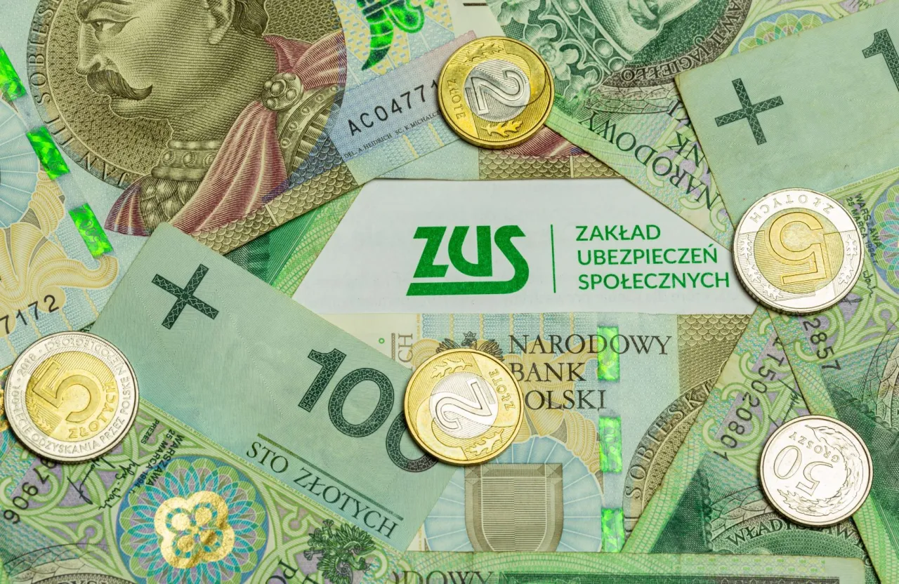 Złotówki i monety na tle logo ZUS. Pamiętaj, kto nie płaci funduszu pracy, może mieć problemy.