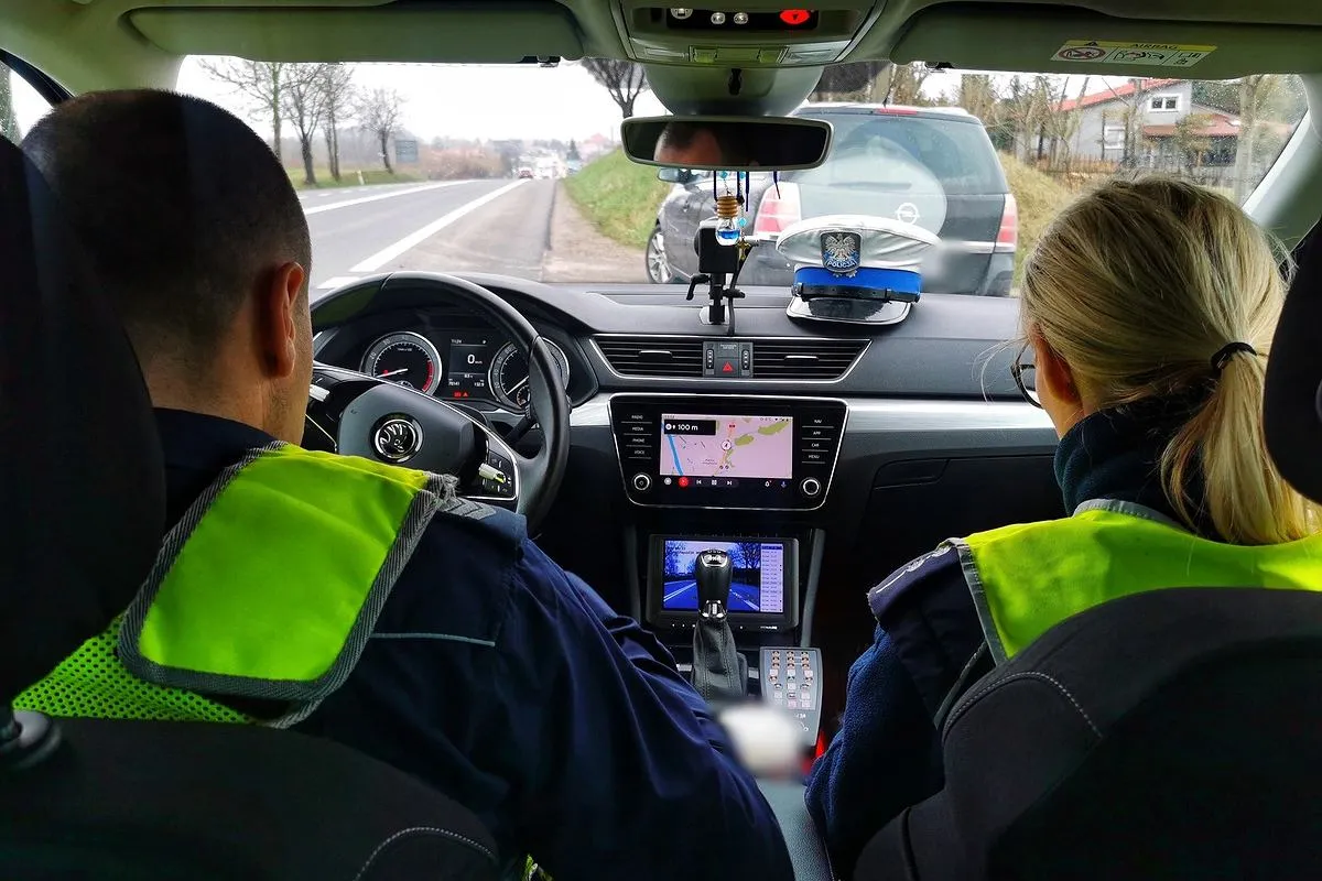 Policjanci w radiowozie monitorują ruch drogowy, gotowi do interwencji w przypadku przekroczenia prędkości.
