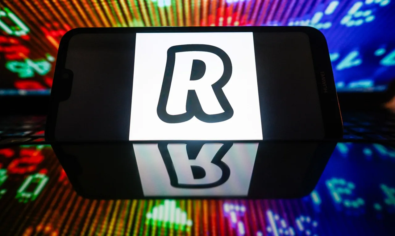 Telefon z logo Revolut. Jak wypłacić kryptowaluty z Revolut? Wyświetlają się wykresy giełdowe.