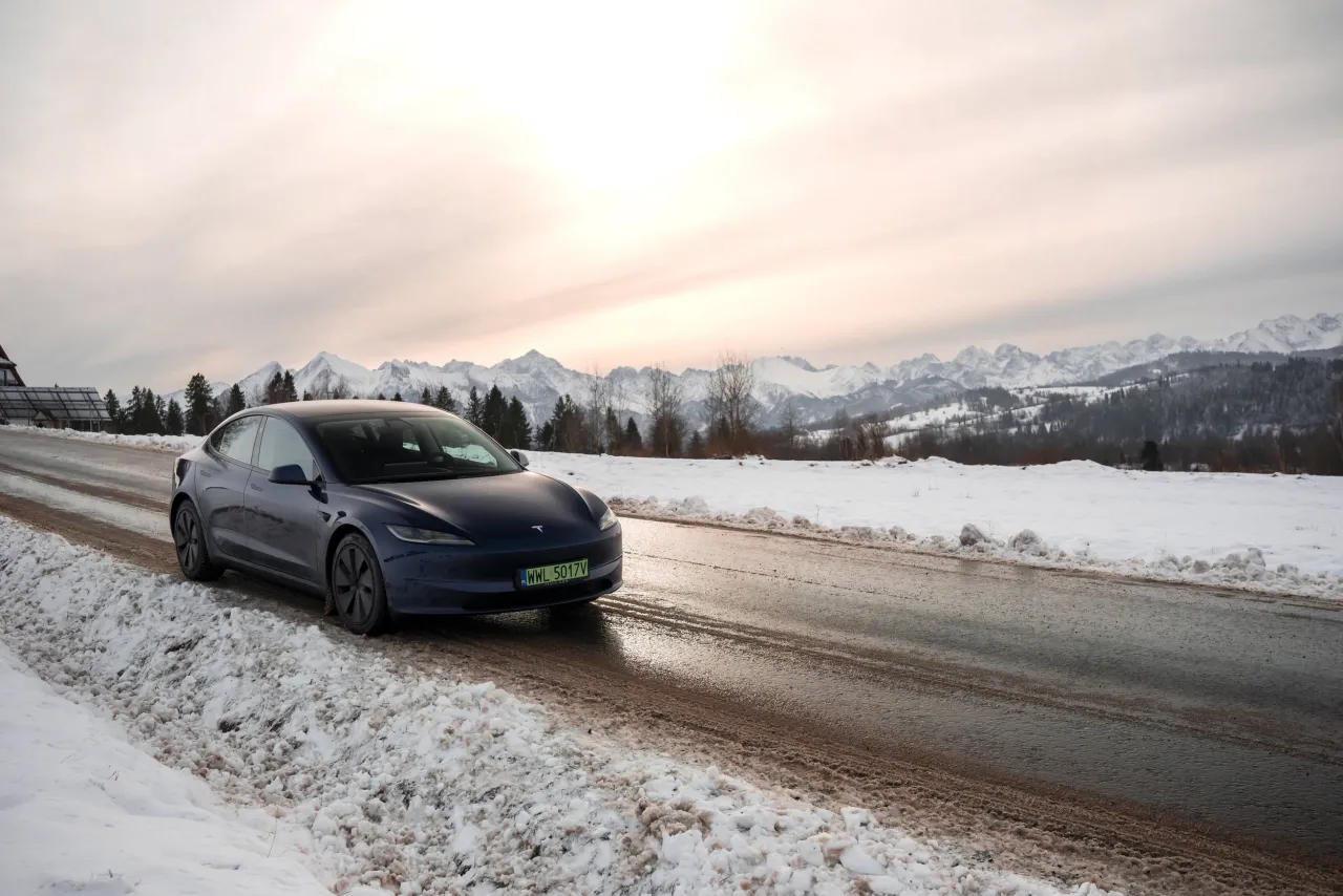 Ciemnoniebieska Tesla na zimowej drodze, za nią ośnieżone g&oacute;ry. Zastanawiasz się, ile przejedzie Tesla na jednym ładowaniu w takich warunkach?