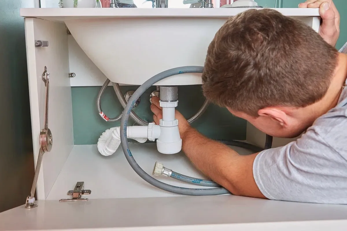 Hydraulik naprawia syfon pod umywalką. Zastanawiasz się, ile kosztuje wizyta hydraulika?