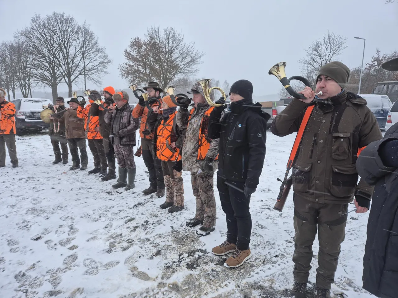 Myśliwi grają na polowaniach sygnałówkę, stojąc w śniegu.
