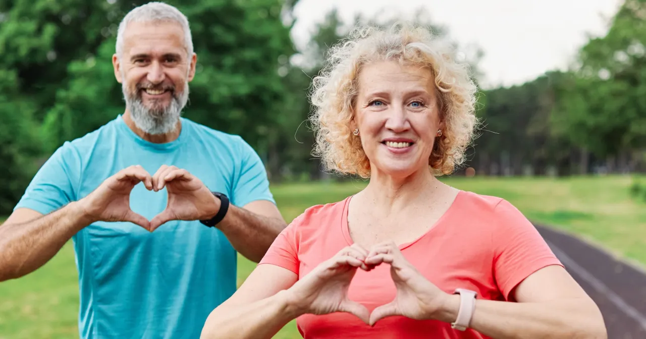 Uśmiechnięci seniorzy pokazują serca dłońmi, symbolizując troskę o zdrowie i jak wzmocnić serce u starszej osoby.