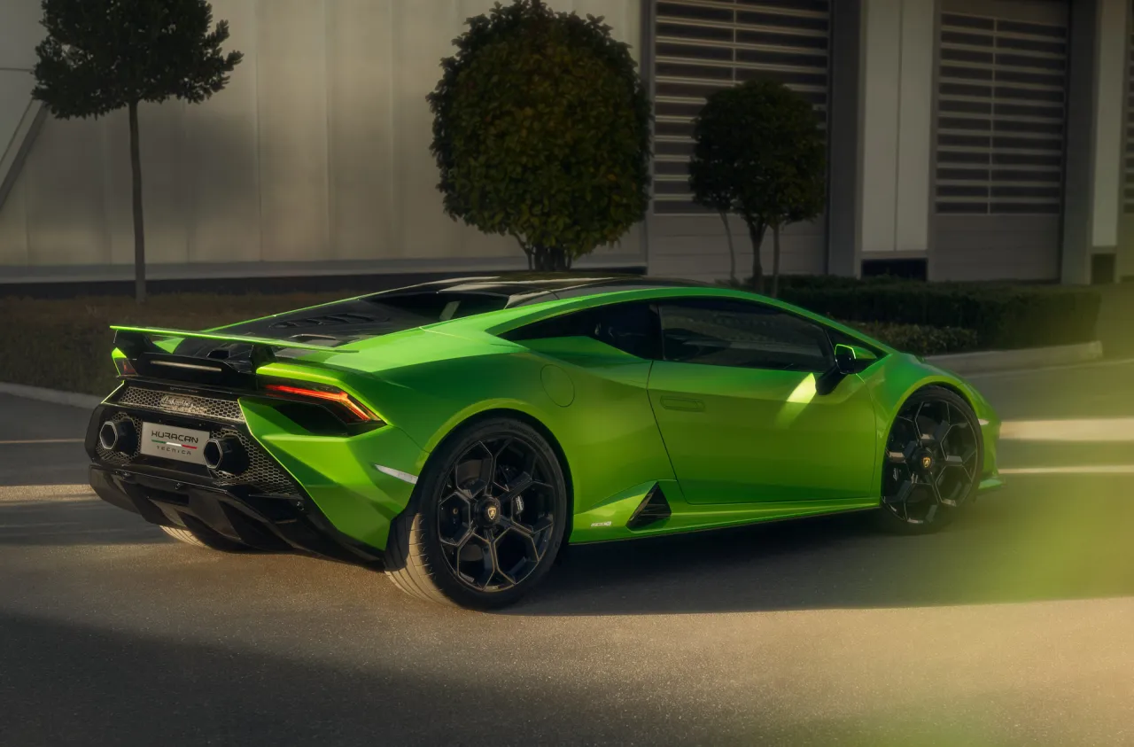 Zielony Lamborghini Huracan Tecnica z czarnymi felgami, zaparkowany przy nowoczesnym budynku.