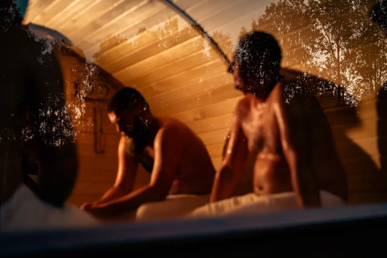 Dw&oacute;ch mężczyzn w saunie, rozmyślających o tym, ile kcal spala sauna. Ciepło i relaks.