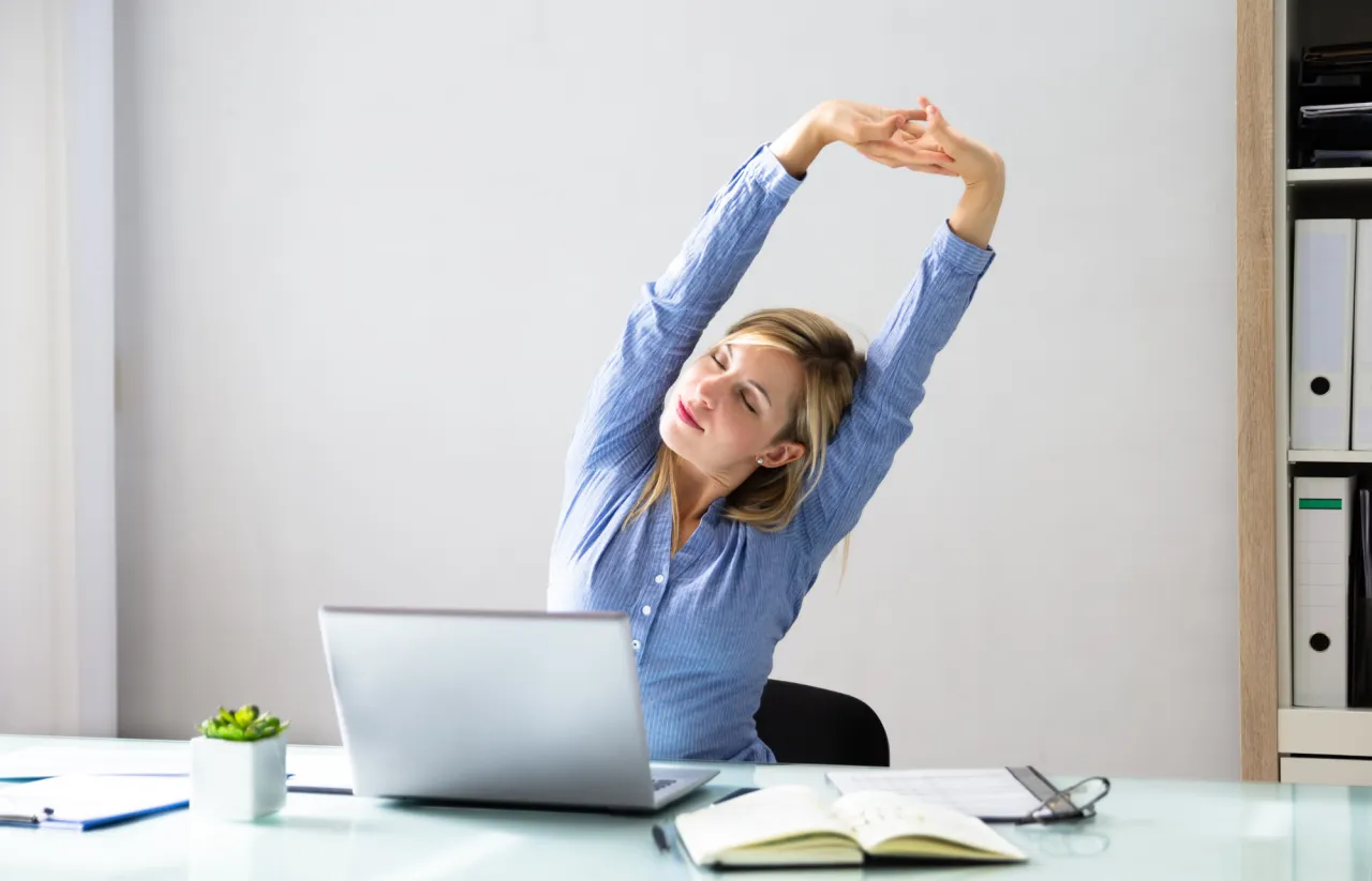 Osoba pracująca przy komputerze i jednocześnie wykonująca proste ćwiczenia rehabilitacyjne