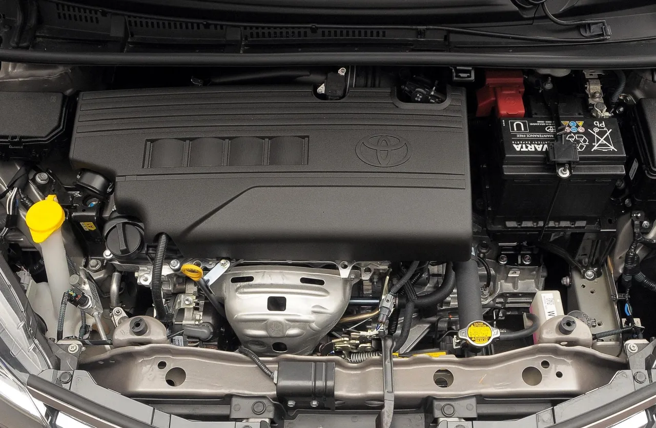 Silnik Toyoty Yaris, widok z góry. Czarna osłona z logo Toyoty, akumulator Varta, płyny i przewody.