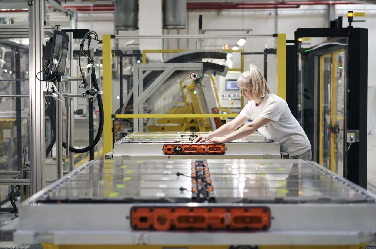 Kobieta pracuje przy linii produkcyjnej, montując moduły baterii do samochodów elektrycznych. Zastanawiasz się, ile kosztuje bateria do samochodu elektrycznego?