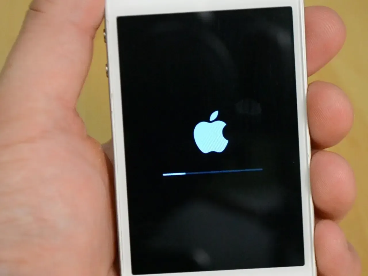 Dłoń trzyma iPhone'a z logo Apple i paskiem postępu. To ekran, który zobaczysz, gdy będziesz próbować jak zresetować iPhone'a.