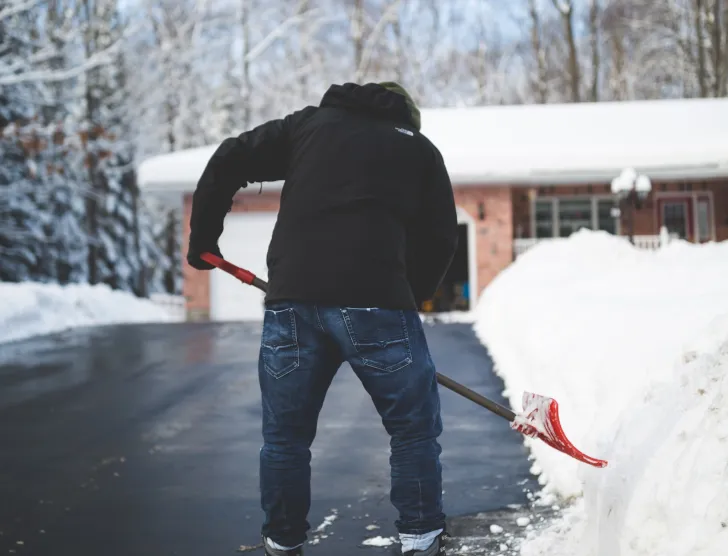 osoba odśnieżająca chodnik przed domem