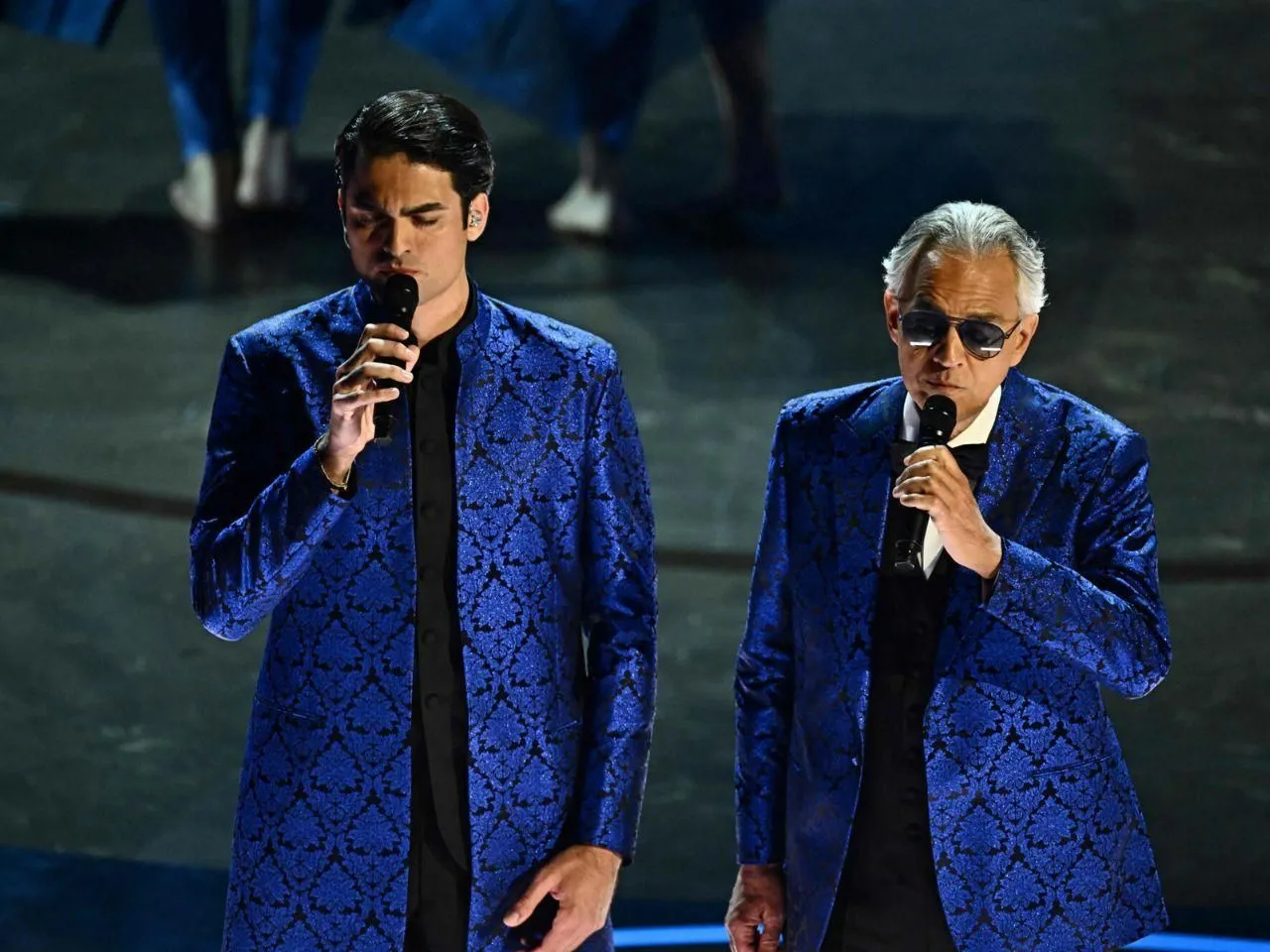 Dwóch tenorów w niebieskich, wzorzystych marynarkach śpiewa do mikrofonów. Zastanawiasz się, ile trwa koncert Andrea Bocelli?