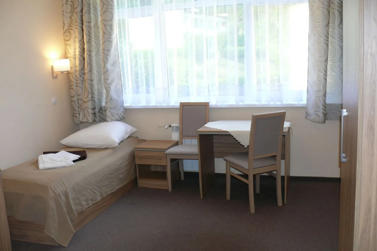 Pokój w sanatorium Leśnik Drzewiarz Krynica Zdrój, ul. Podgórna 1. Łóżko, stolik, krzesła i okno.