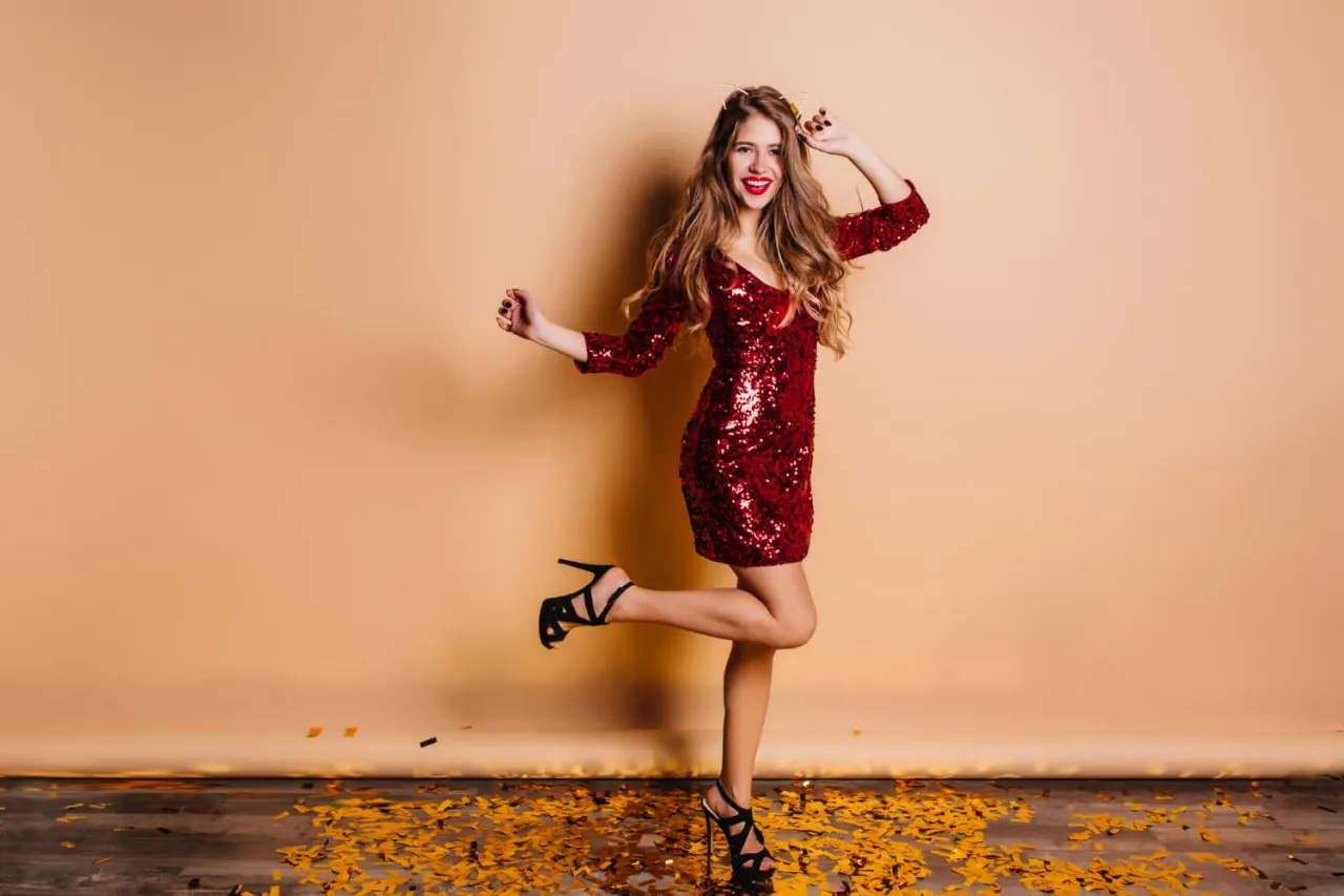 Kobieta w czerwonej, cekinowej sukience i czarnych szpilkach. Idealny przykład, jak dobrać buty do sukienki wieczorowej, by stworzyć olśniewającą stylizację.