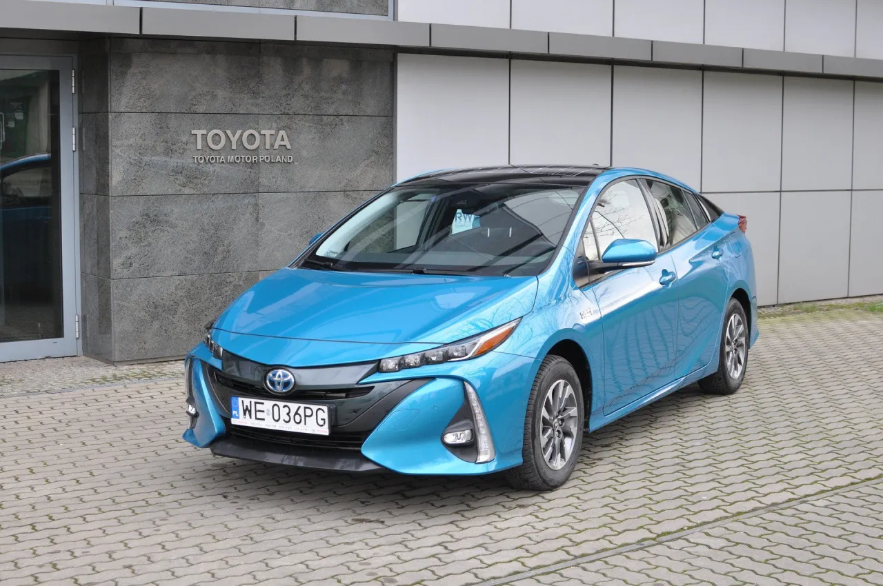 Niebieska Toyota Prius przed budynkiem Toyoty. Zastanawiasz się, ile pali Toyota Prius? Ten model słynie z niskiego spalania.