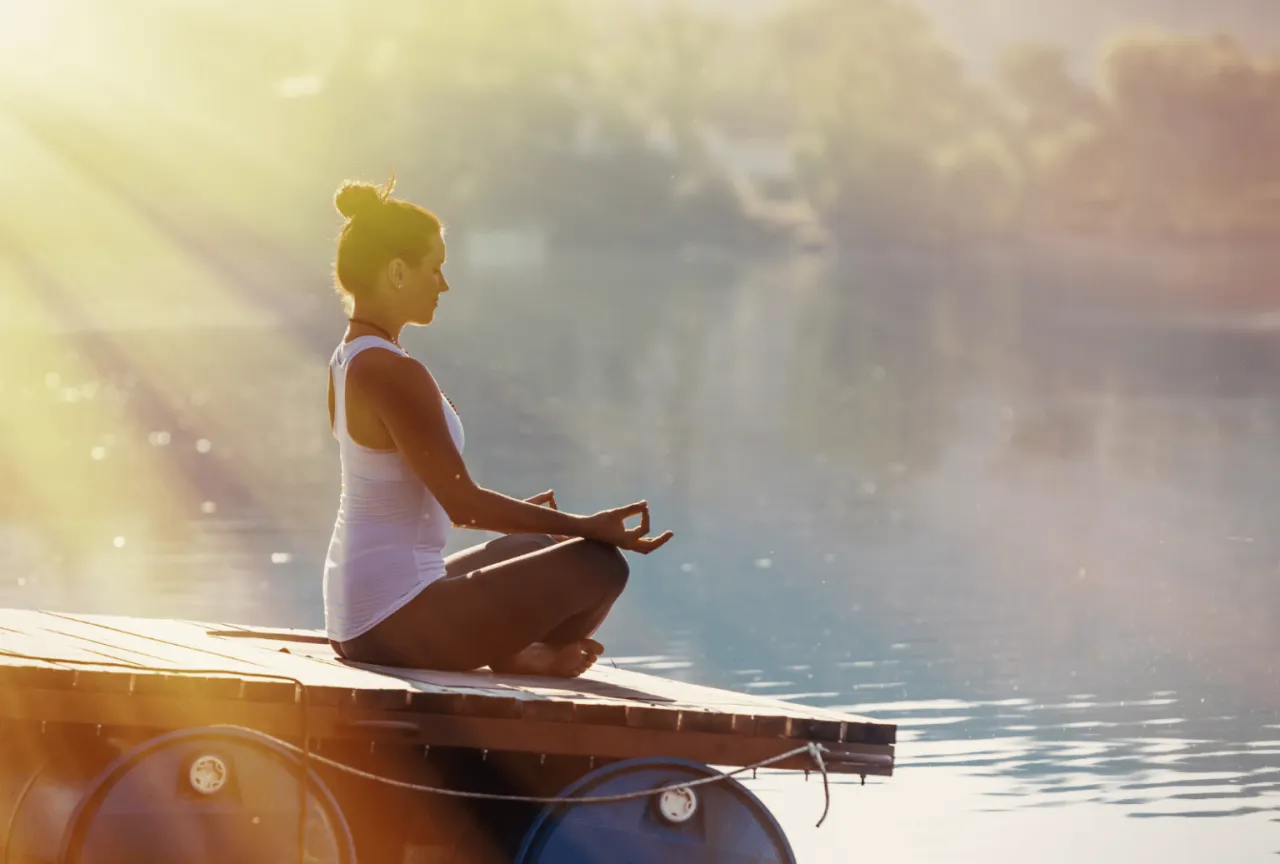 Kobieta medytuje na pomoście przy jeziorze. To kwintesencja