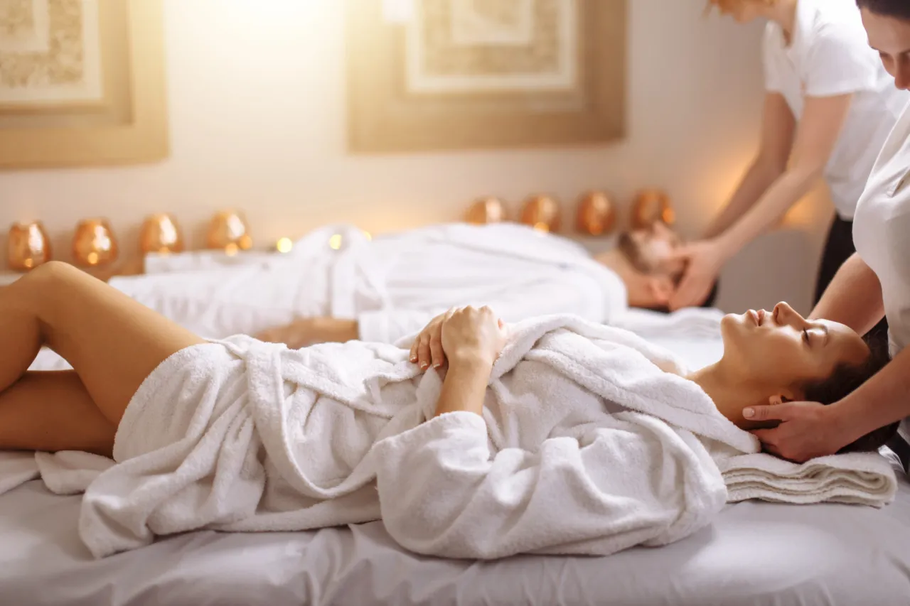 Relaks w spa w Rudzie Śląskiej. Kobieta w białym szlafroku leży na masażu, podczas gdy masażystka delikatnie uciska jej głowę.