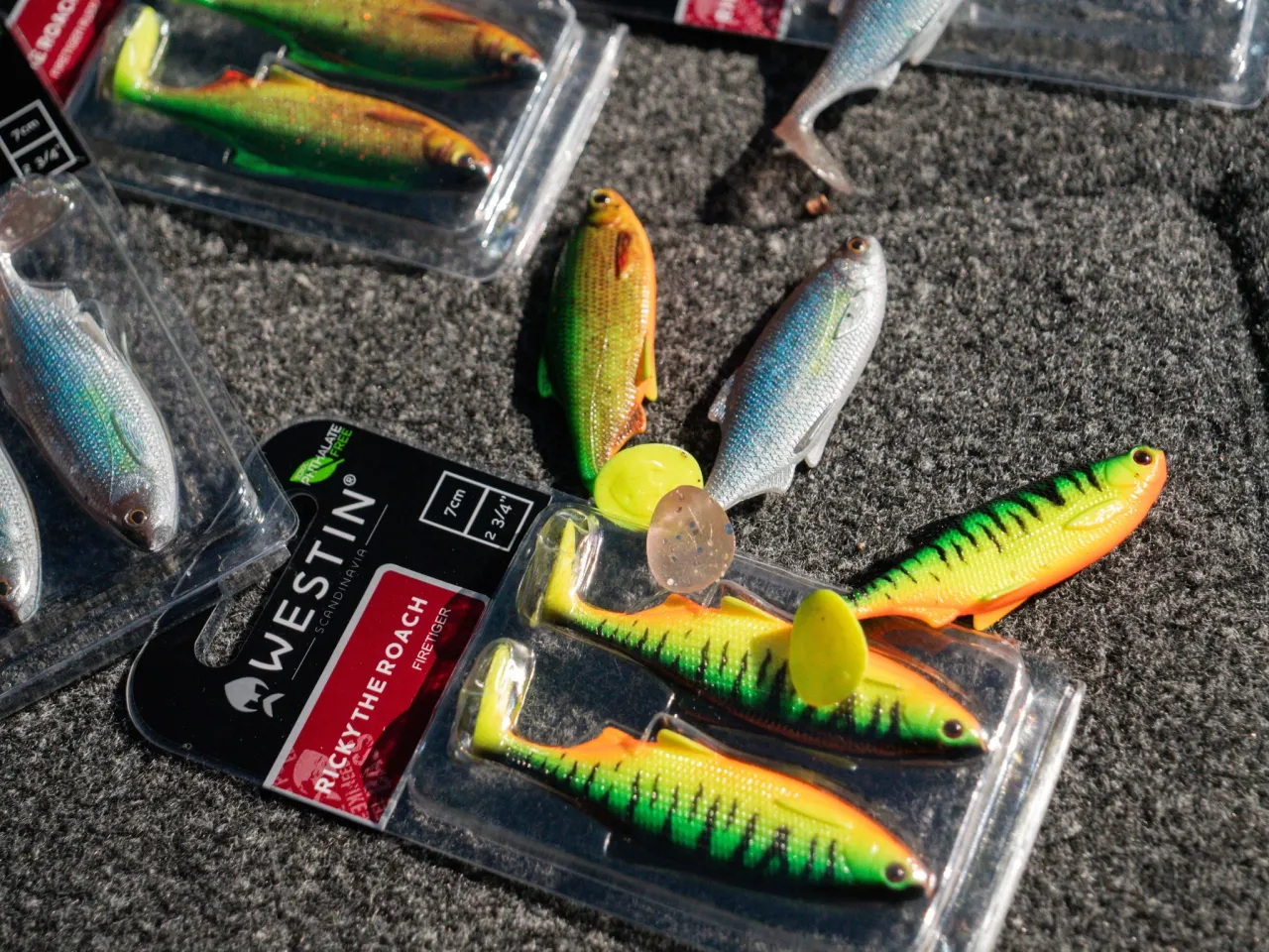 R&oacute;żnorodne jakie przynęty na ryby: gumowe imitacje rybek w opakowaniach, w kolorach zielonym, ż&oacute;łtym i srebrnym, gotowe do połowu.