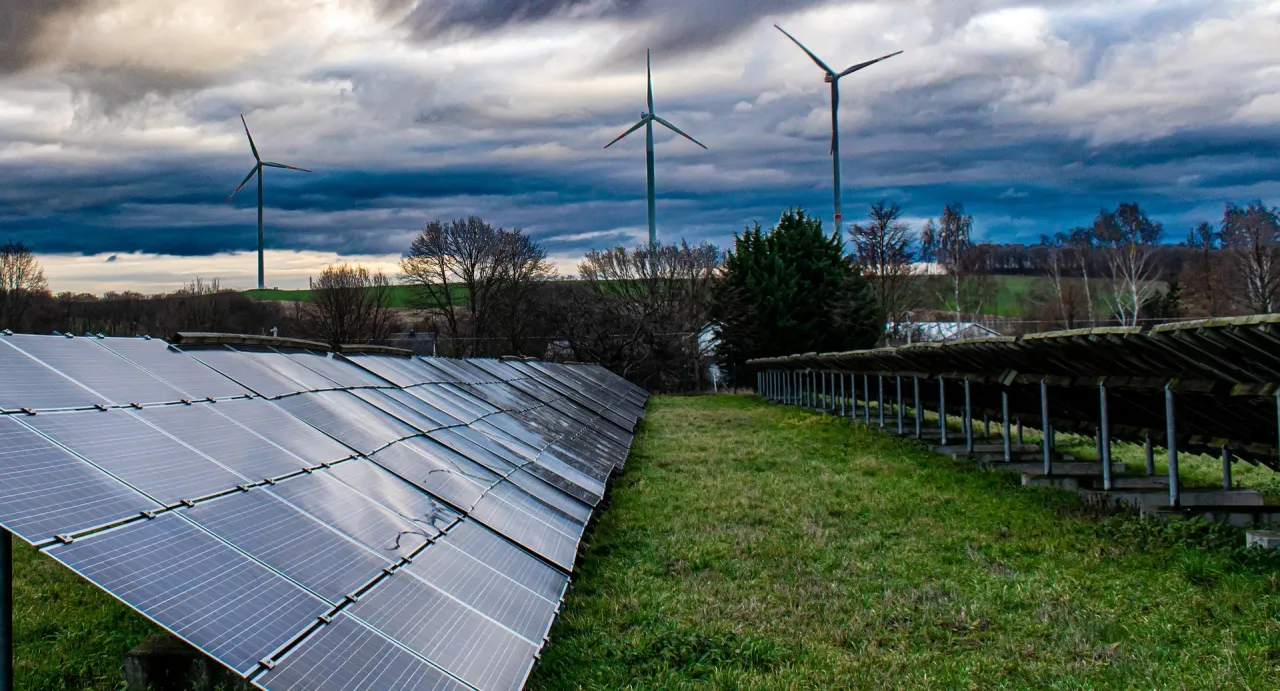 Panele słoneczne i wiatraki na tle burzowego nieba. Nowelizacja ustawy o OZE nabiera tempa.