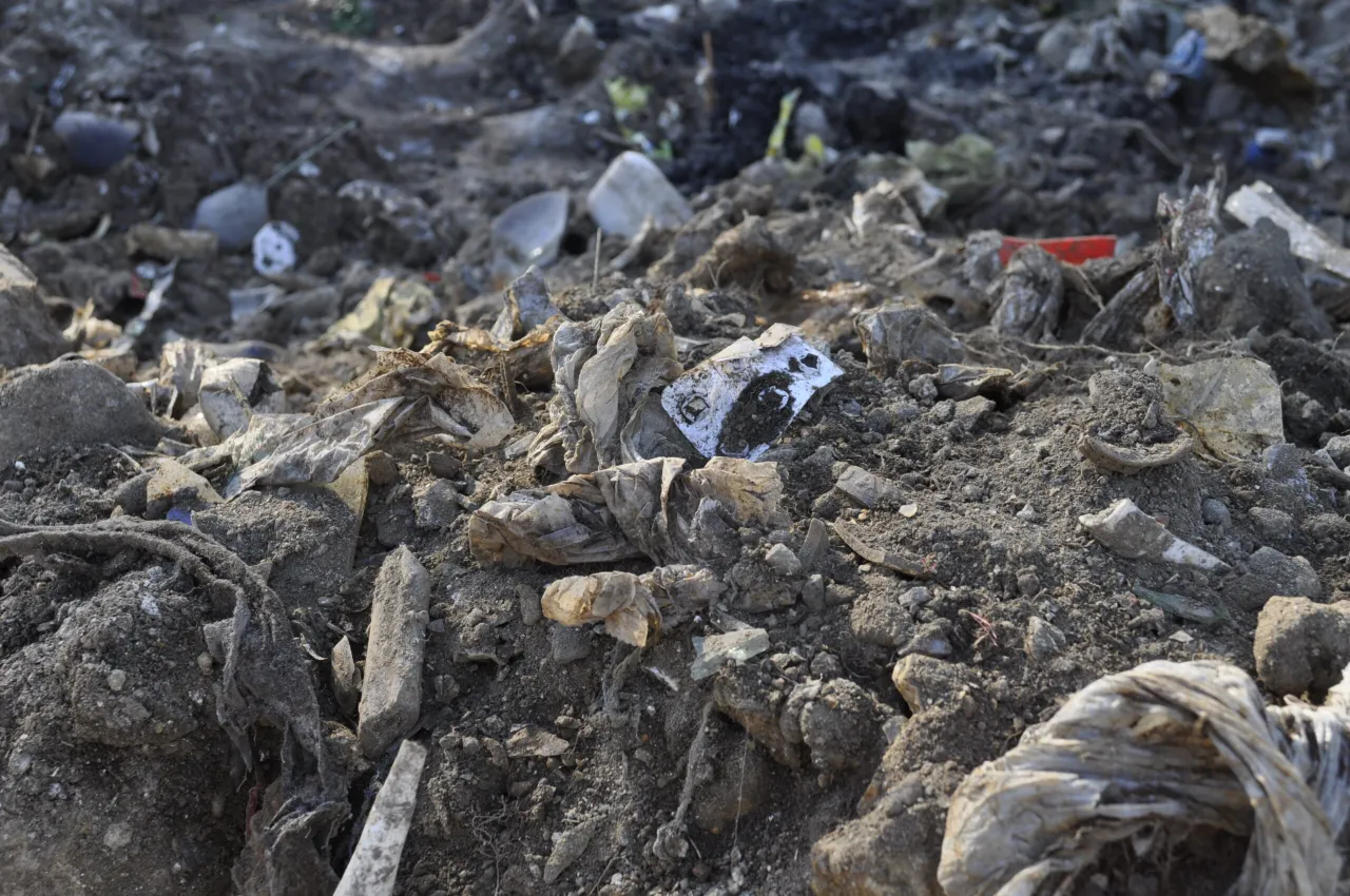 Zanieczyszczona gleba z plastikiem i gruzem. Pokazuje, jak chronić glebę przed zanieczyszczeniami, unikając takich widok&oacute;w.