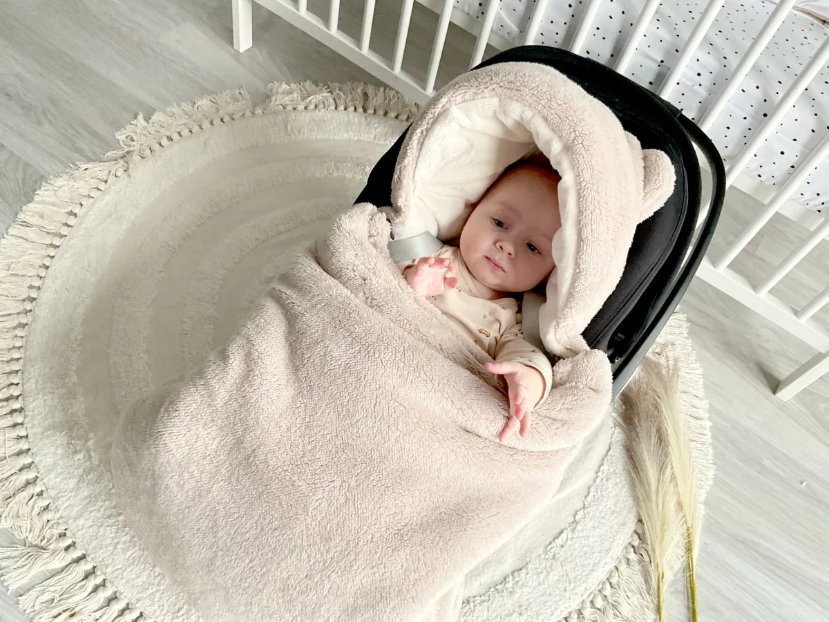 Ciepły, pluszowy kombinezon do fotelika samochodowego otula maluszka. Urocze uszka dodają mu uroku.