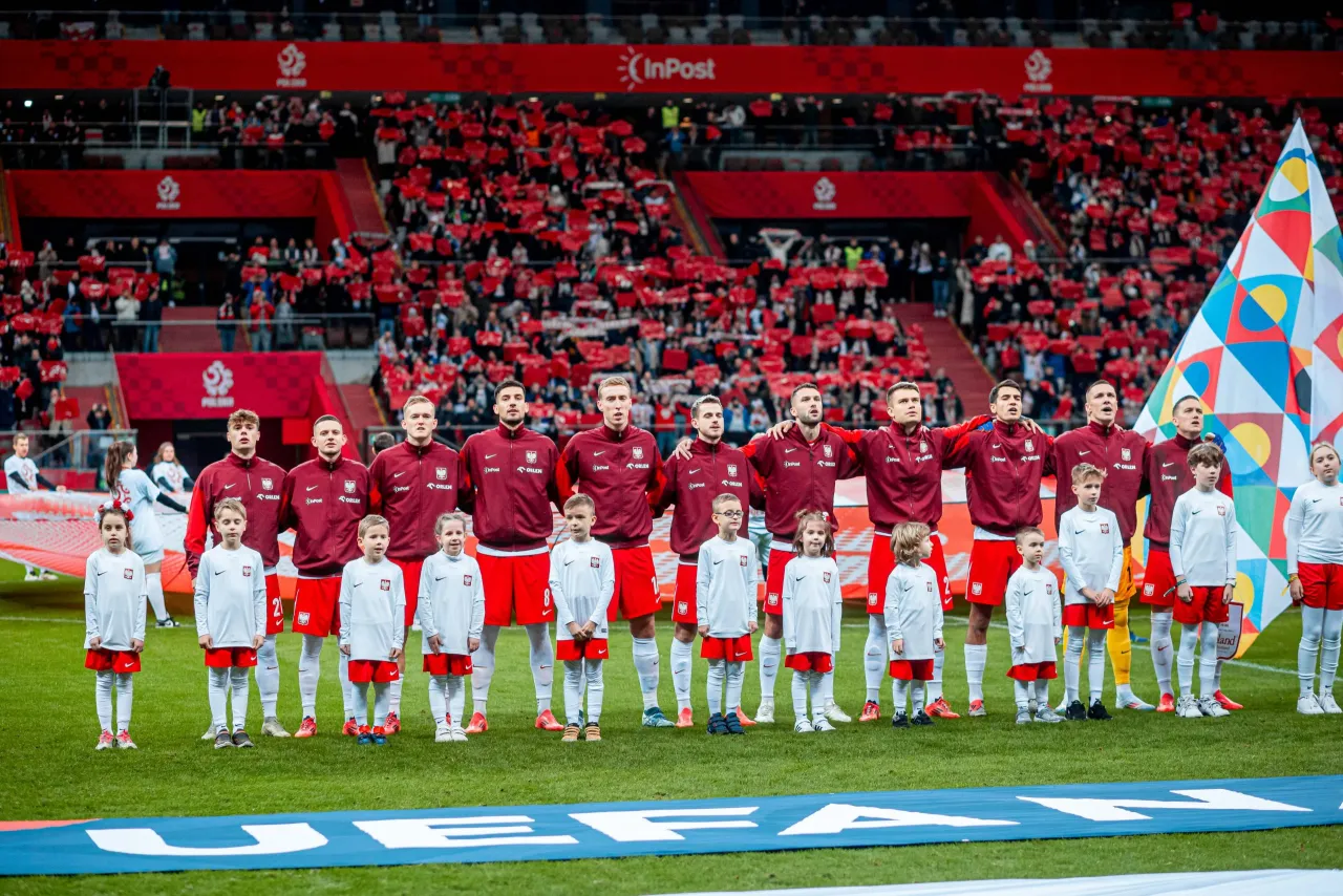 Piłkarze reprezentacji Polski i dzieci stoją na murawie stadionu, gotowi do meczu. Tłumy kibic&oacute;w na trybunach czekają, kiedy gra polska w piłkę nożną.