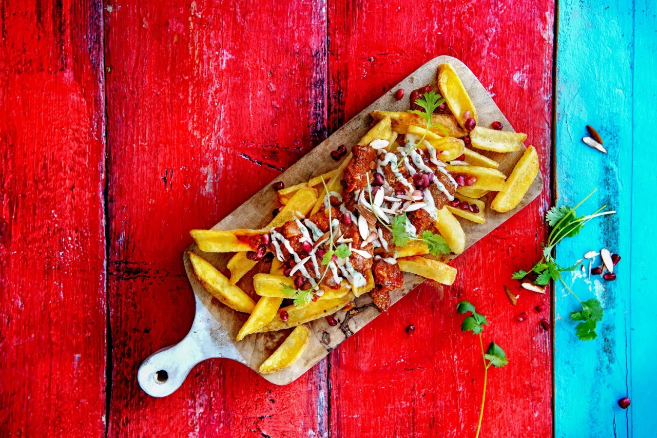 Idealne co do frytek na szybko: złociste frytki z mięsem, granatem, migdałami i sosem na czerwonym tle.