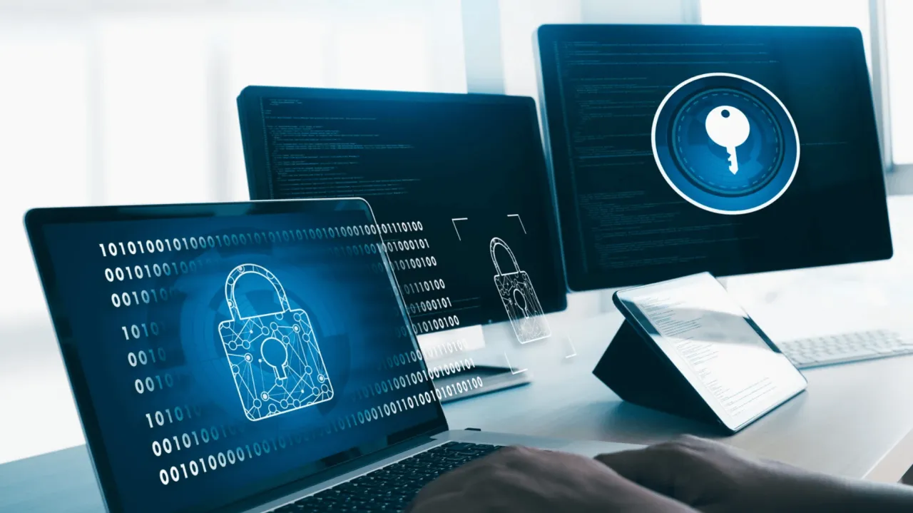 Komputery i tablet z ikonami kł&oacute;dki i klucza, kod binarny na ekranach. Aktualizacja systemu bezpieczeństwa.