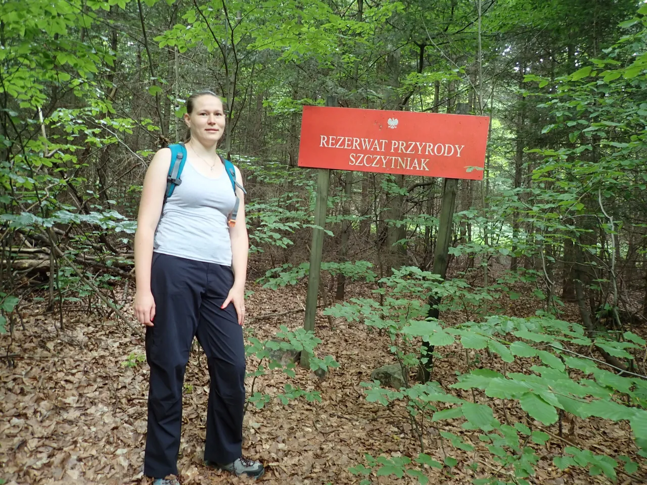 Kobieta stoi obok znaku informującego o rezerwacie przyrody Szczytniak.