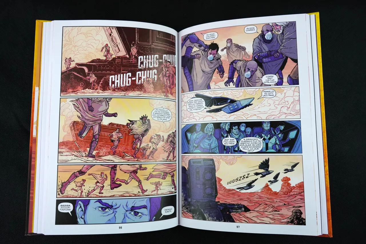 Otwarta księga z ilustracjami komiksowymi. Postacie w strojach z maskami biegną przez pustynny krajobraz. Czy komiks to książka? Tak, to opowieść w obrazach.